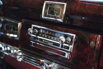 Luxury interior of old classic American car. Wooden decorated dashboard with radio and clocks.