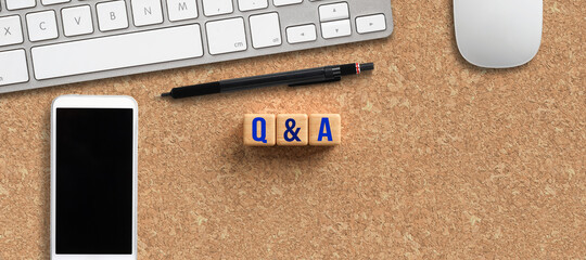 cubes with message Q&A and smartphone, pen and computer keyboard on cork background