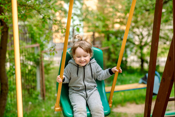 Laughing child on swing in summer park.plays children's games, runs and jumps. carefree childhood.