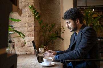 Brunette man working in cafe with computer and coffee