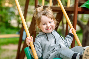 Laughing child on swing in summer park.plays children's games, runs and jumps. carefree childhood.