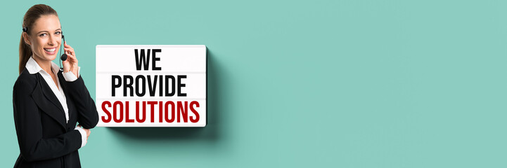 businesswoman with a headset in front of a wall with lightbox and message WE PROVIDE SOLUTIONS