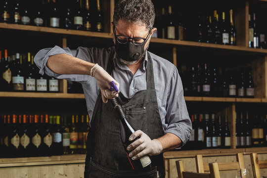  a bartender opens a bottle of red wine wearing a protective mask due to the coronavirus pandemic. Safety reopening of restaurants after the covid-19 lockdown.
