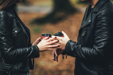 Cropped photo of couple holding paper coffee cups, touching one another hands in autumn park.
