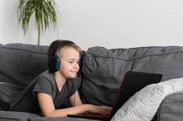 Happy boy in headphones playing or studying on laptop computer at home. Child use pc.