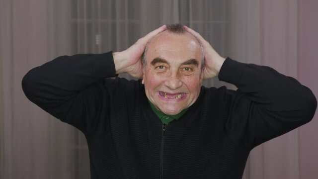 Senior man scares rubbing his head , opening his toothless mouth wide. Close-up portrait.