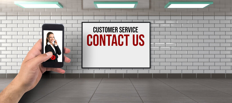 hand holding smartphone ready to call businesswoman in front of a billboard with the text CUSTOMER SERVICE - CONTACT US