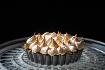 An individual lemon meringue pie in a tart dish on a glass dish.  Dark background with space for copy text 