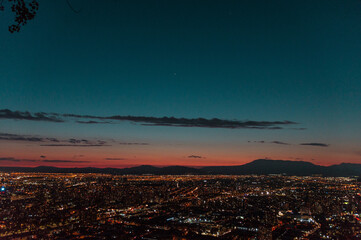 Ciudad de noche con luces encendidas entre montañas en el horizonte