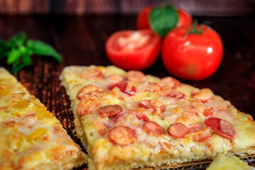 Closeup pizza slice with cabanossi, ham and cheese on brown wooden background