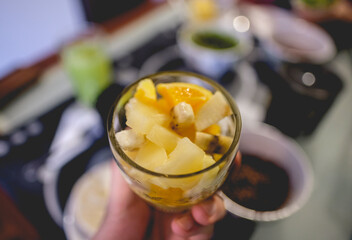 Hand holding a glass cup with chopped fruit salad of orange, apple, pineapple and banana