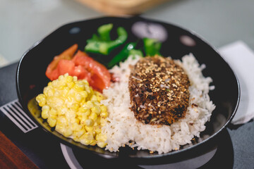 Vegetable hamburger with corn with vegan mayo, white rice, tomato and peppers in a black plate in home
