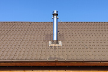 A steel metal pipe with wind protection is mounted on ropes on a brown roof covered with metal close up