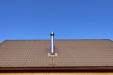 A steel metal pipe with wind protection is mounted on the cables in the center of the brown roof covered with metal.