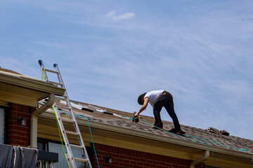 Construction worker roofer builder on roof structure applying asphalt shingles roofing