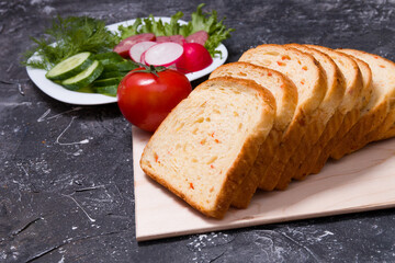 bread for toast with slices of vegetables lies on a wooden cutting board, in the background ingredients for a sandwich, vegetables and sausage are cut on a plate