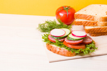 a sandwich of vegetables and diet sausages on the table, yellow background, bread and vegetables in the background, healthy breakfast concept