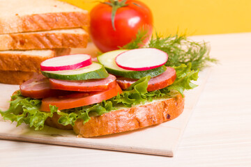 a sandwich of vegetables and diet sausages on the table, yellow background, bread and vegetables in the background, healthy breakfast concept