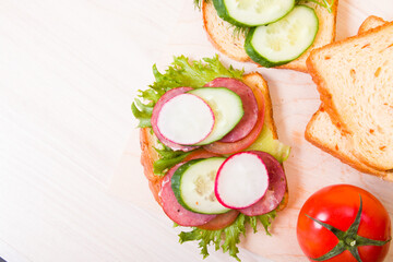 a sandwich of vegetables and diet sausage on a wooden cutting board, wooden table, bread and vegetables in the background, healthy breakfast concept, copy space