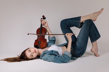 The girl in jeans and barefoot plays the violin on a white background