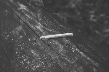 Black and white photo of a smoking and smoldering cigarette on a wood background
