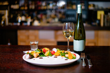 Mussel salad on a white plate with glass and bottle of wine on the background of the bar. Concept of a beautiful dish serving for a restaurant.