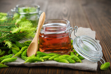 Jar of  jam, syrup or honey from fir buds and needles, twigs of fir tree on wooden table. Making...