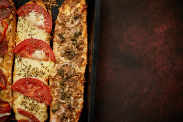 Long baguettes pizza sandwiches with tuna, mushrooms, tomatoes and cheese on a metal baking tray