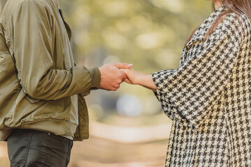 Cropped photo of couple in love holding hands in autumn nature with sunrays everywhere.