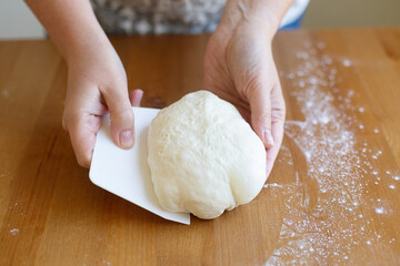 Female hands cut with a scrapper a kneaded dough on a wooden table. The process of preparing fresh elastic baking dough for pizza or bread. Table and hands in flour. Natural home healthy cooking, dayl