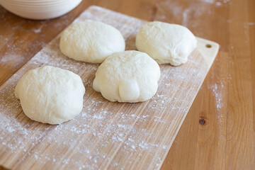 Fototapeta na wymiar A round pieces of homemade white dough for pizza, bread or baking goods on a wooden cutting board. Small pieces of dough ready to be baked. Healthy natural family food. Side view, daylight, home 