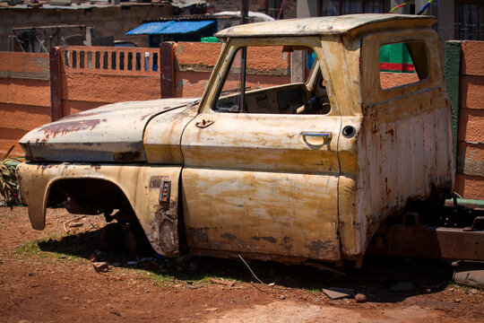 The front half of a rusty old truck sits in front of a wall in Alexandra Township, South Africa.