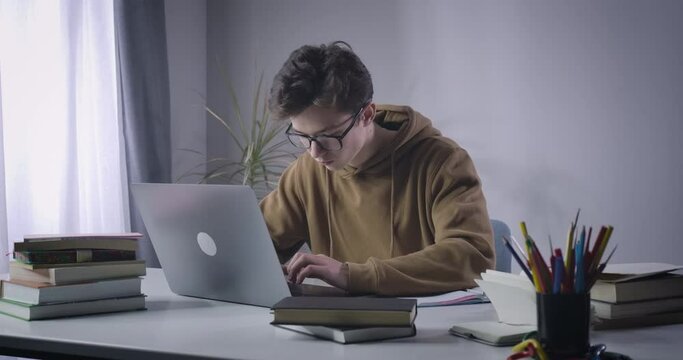 Excited Caucasian nerd boy typing fast on laptop keyboard. Absorbed college student searching information for project in Internet. Education, diligence, studying. Cinema 4k ProRes HQ.