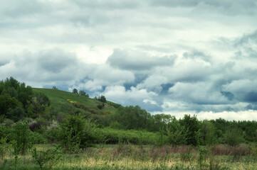 Fluffy clouds over beauty spring hills and green valley. True wild nature landscape