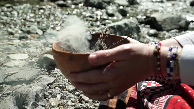 A female shaman sangoma holding a burning bowl to honor her ancestors near a mountain stream