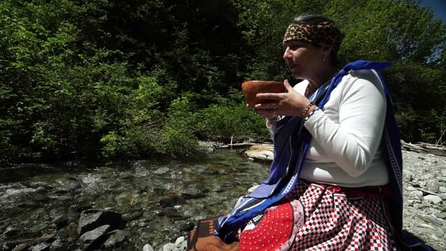 A beautiful female shaman sangoma offering burning plant medicine to honor her ancestors near a mountain stream