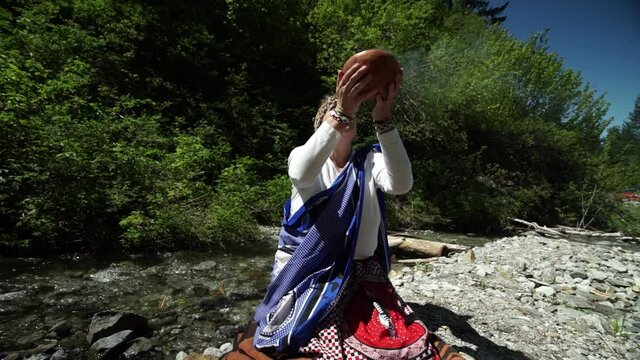 Looking up at a female shaman sangoma raising burning plant medicine to honor her ancestors near a mountain stream