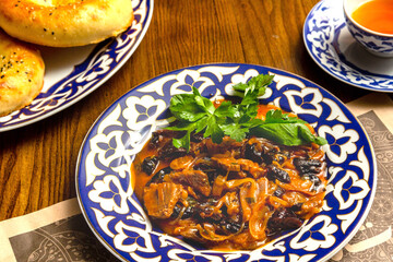 Traditional oriental meat dish with vegetables in painted plates on a plate on a table in a restaurant