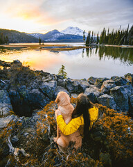 Girl with a dog sitting near the lake and watching sunset