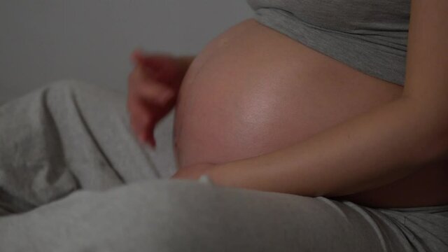 Pregnant Woman on 38th week sitting on the home bed and touching belly pregnancy line On Her tummy with one finger. - close up profile shot