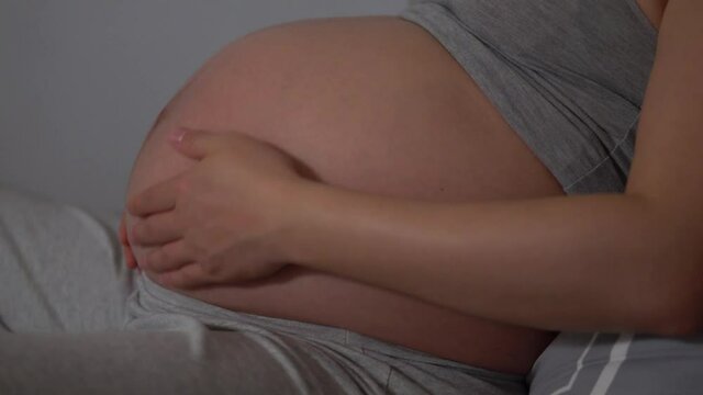 Pregnant Woman sitting on the bed and Rubbing On Her Belly. - close up profile shot