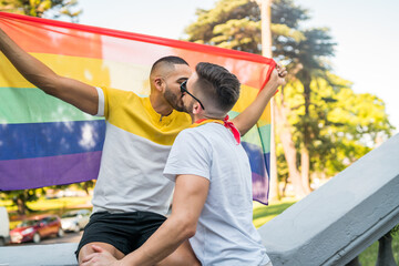 Obraz premium Gay couple kissing and showing their love with rainbow flag.