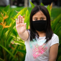 Young  kid wearing anti-virus protection mask. Reusable black face mask. Raising hand showing do not get close to prevent the spread of the virus in the park. Social Distance concept focus on hand