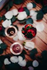 Glasses of rose wine surrounded by petals with chocolate covered strawberries