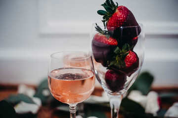 Glasses of rose wine surrounded by petals with chocolate covered strawberries