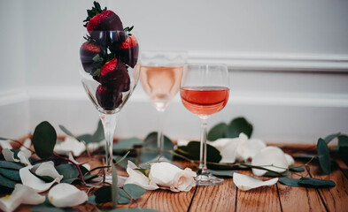 Glasses of rose wine surrounded by petals with chocolate covered strawberries