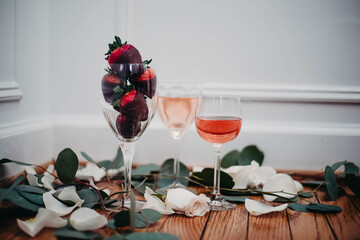 Glasses of rose wine surrounded by petals with chocolate covered strawberries