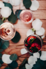 Glasses of rose wine surrounded by petals with chocolate covered strawberries