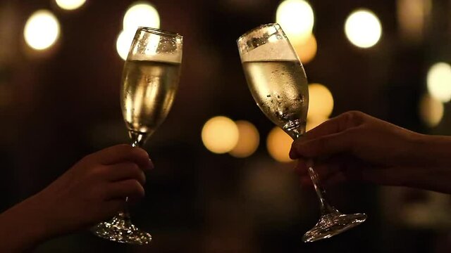 slow motion of two hands holding drinking glass, cheers in darkness. Golden bokeh background