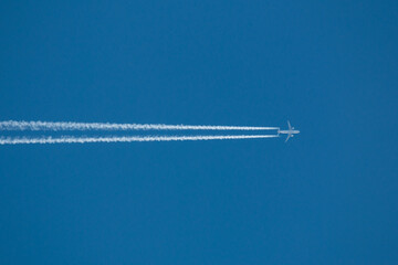 Airplane flying at high altitude leaving its white wake over blue sky